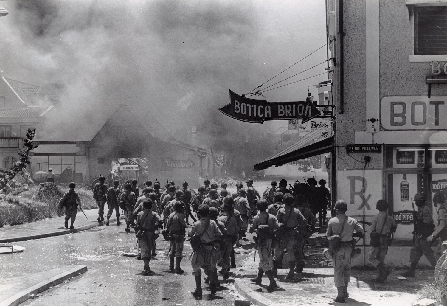 Foto van mariniers die een brandende wijk van Willemstad intrekken (hoek De Rouvilleweg) tijdens de opstand op Curaçao in 1969