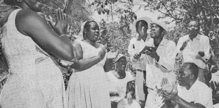 Foto van een groep Antilliaanse mannen en vrouwen die Tambú zingen en dansen