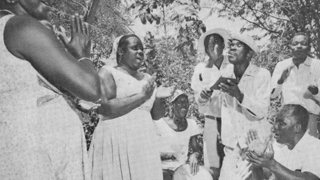 Foto van een groep Antilliaanse mannen en vrouwen die Tambú zingen en dansen